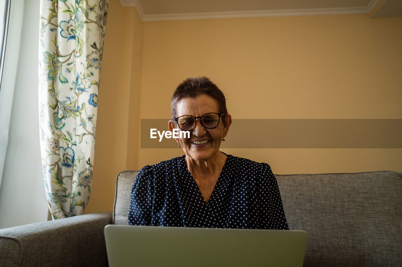 Smiling senior woman sitting at home office workplace looking in laptop.