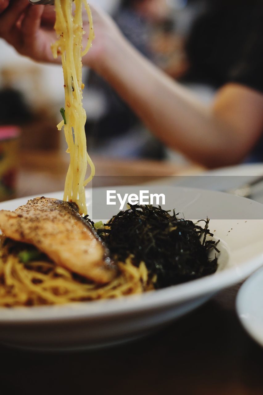 Cropped image of person having spaghetti on table