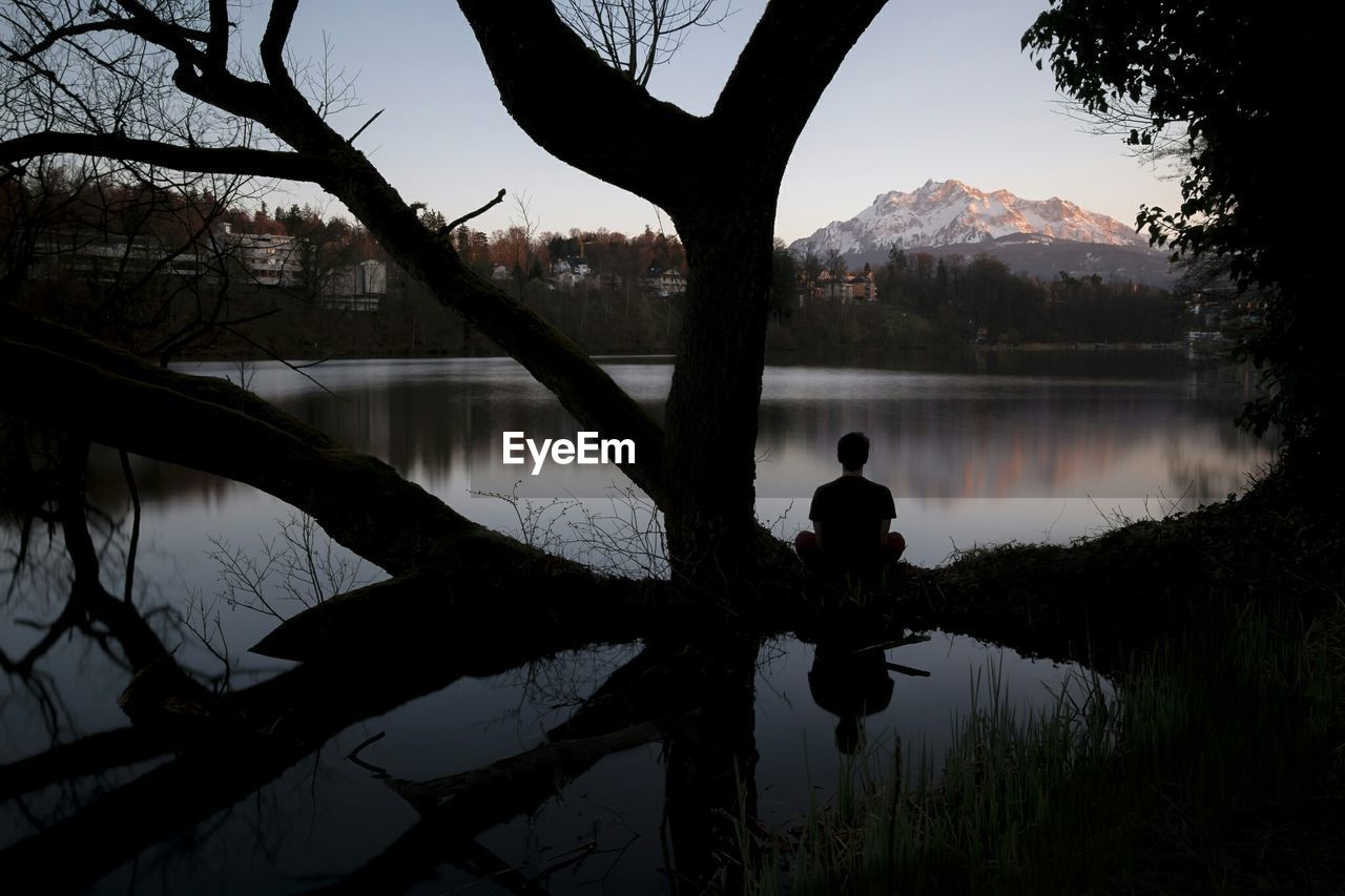 Man meditating by water at dusk