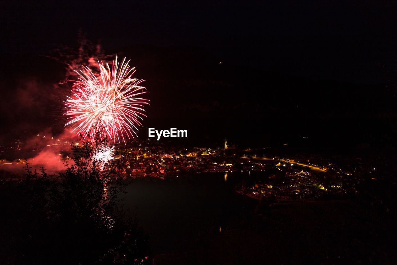 FIREWORK DISPLAY OVER ILLUMINATED CITYSCAPE AGAINST SKY AT NIGHT