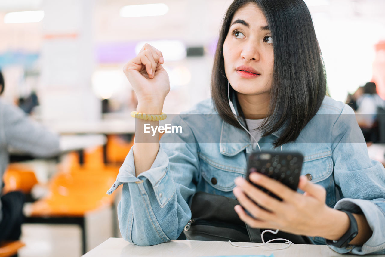 Young woman listening music while using phone at table