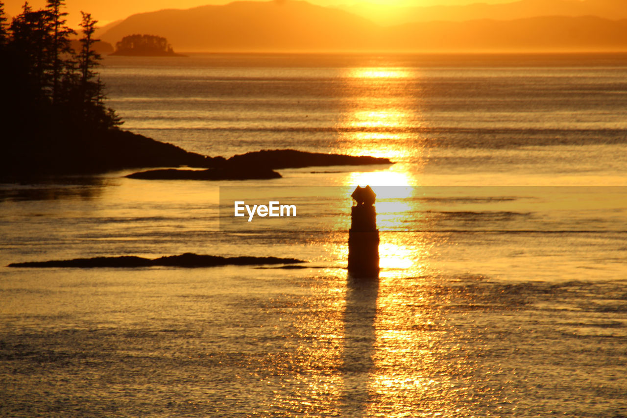 water, sunset, sea, sky, beach, beauty in nature, silhouette, land, orange color, nature, horizon, scenics - nature, one person, sunlight, ocean, reflection, shore, sun, tranquility, dawn, tranquil scene, horizon over water, idyllic, leisure activity, lifestyles, men, afterglow, wave, standing, vacation, coast, holiday, body of water, outdoors, trip, motion, adult, evening, full length, non-urban scene