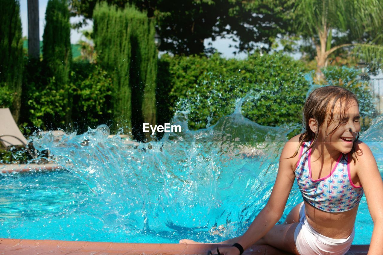 Water splashing on girl at poolside during sunny day