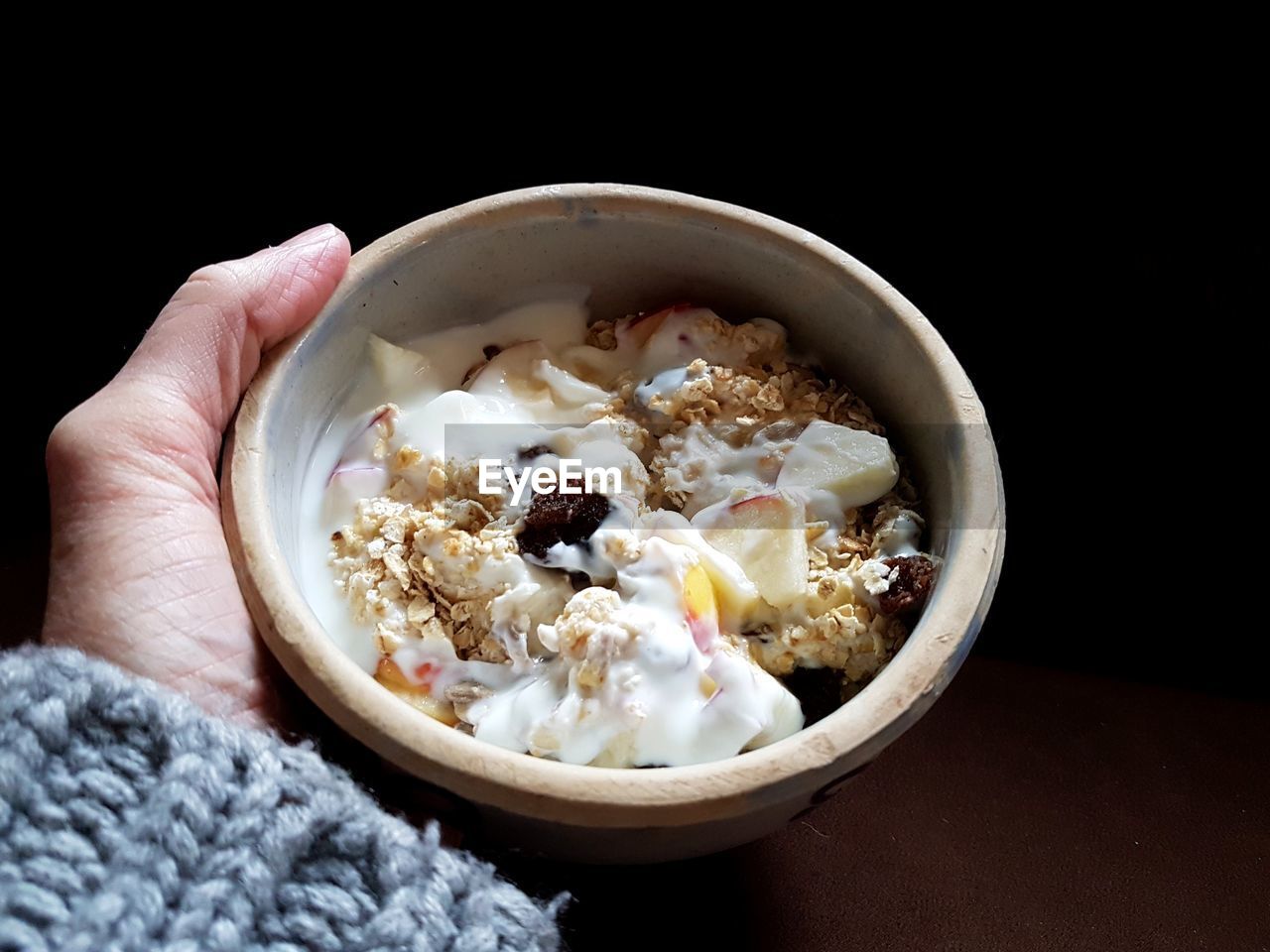 Cropped hand holding bowl with food over black background