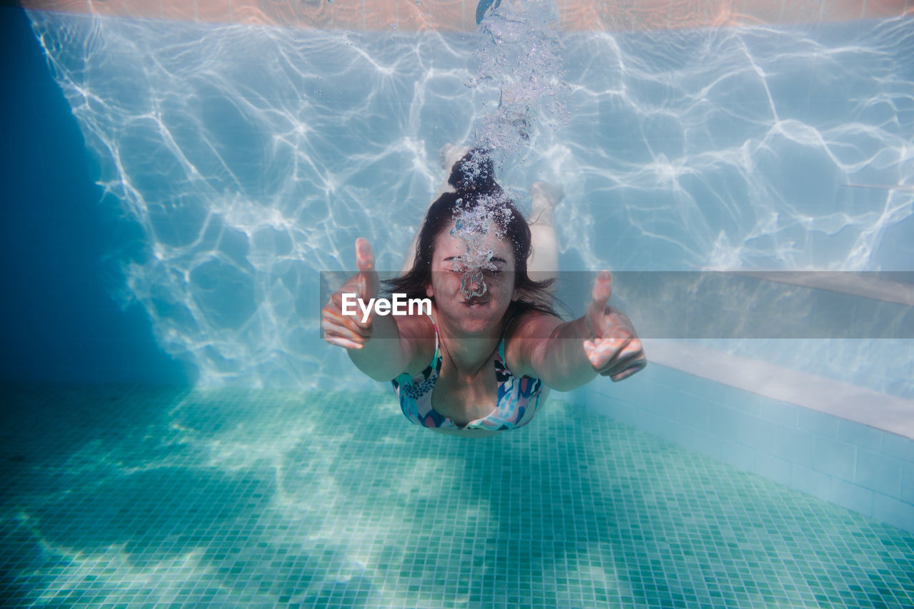 Woman gesturing while swimming underwater in pool