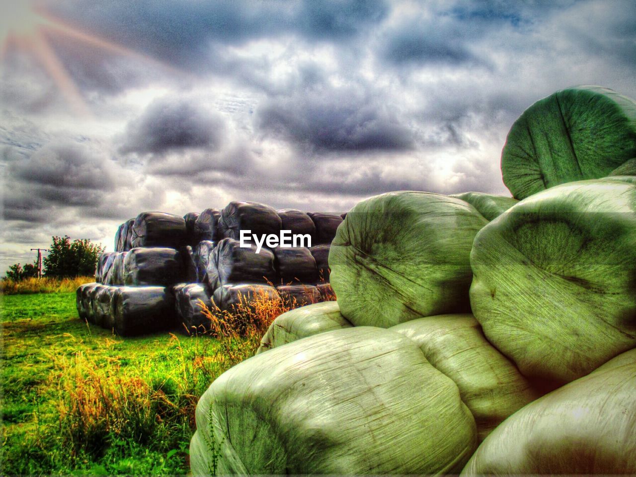 Stack of covered hay bales on field against sky