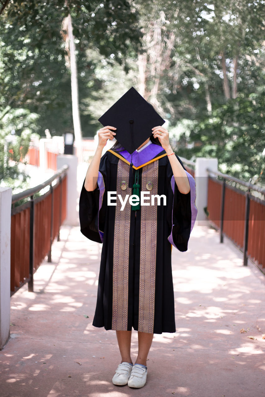 Full length of woman holding mortarboard on street