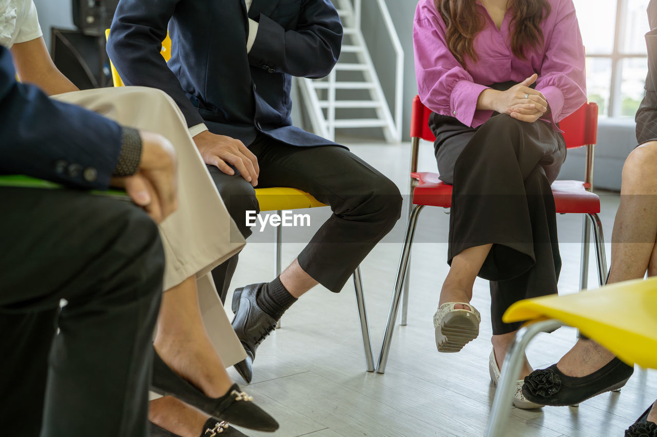 A group of people sitting in chairs, one of whom is wearing a pink shirt. scene is casual