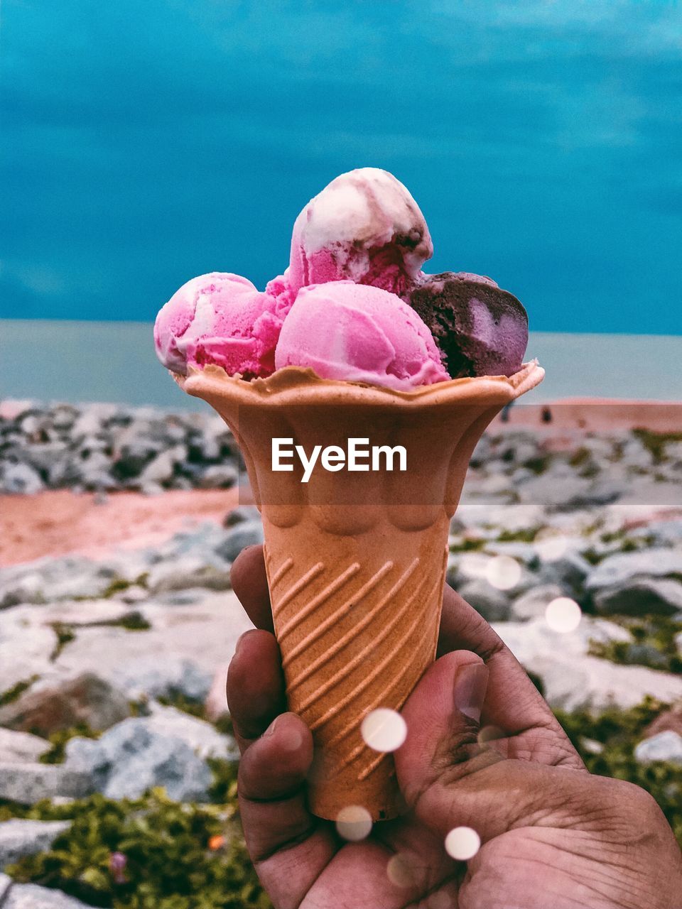 Cropped hand of person holding ice cream against sky