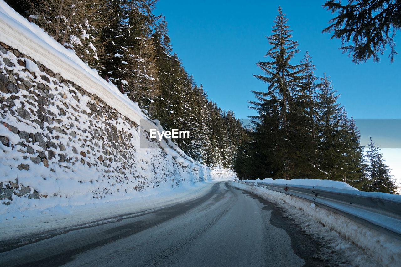 Snow covered road by trees against sky