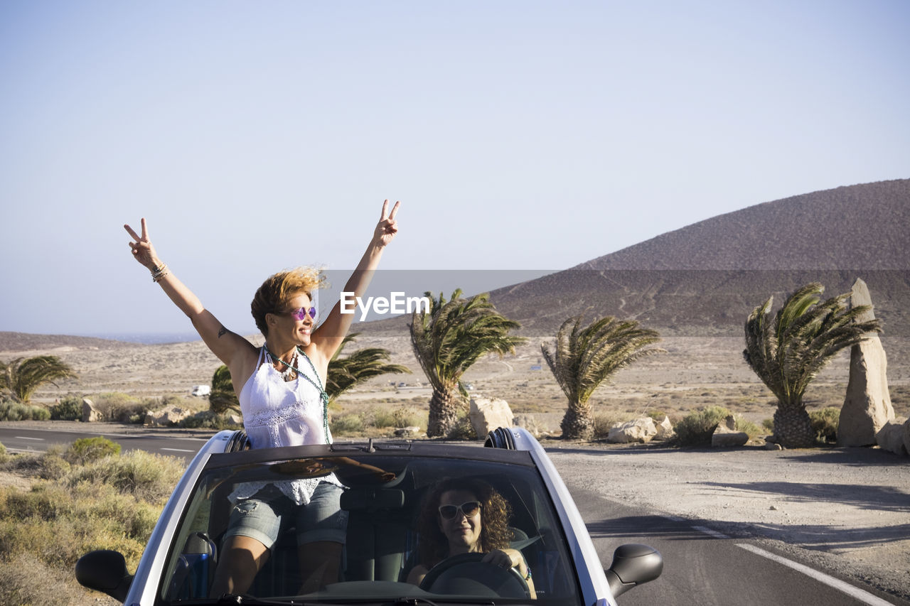 Happy female friends wearing sunglasses standing in convertible against clear sky