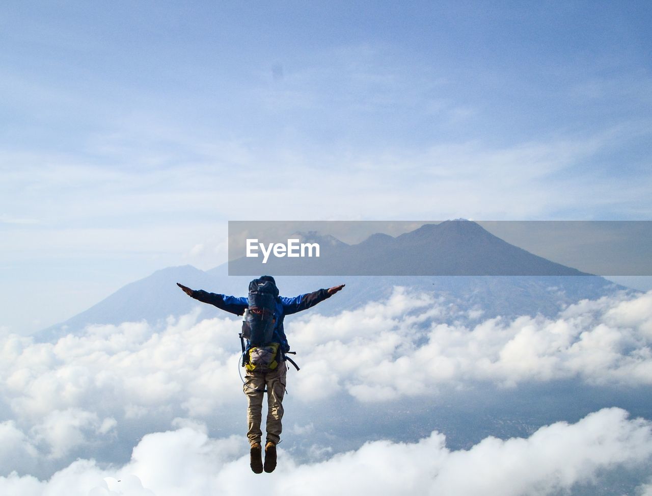 Rear view of person with arms outstretched in mid-air against mountains