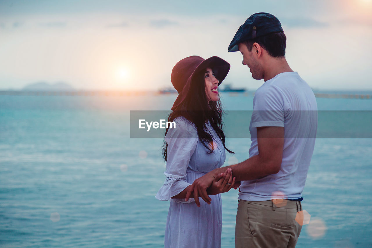 COUPLE STANDING ON SEA SHORE AGAINST SKY