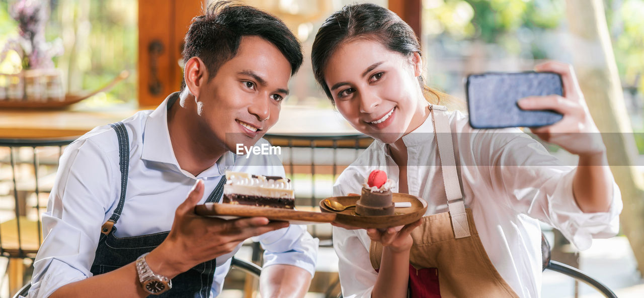 Cheerful couple holding cake while doing selfie