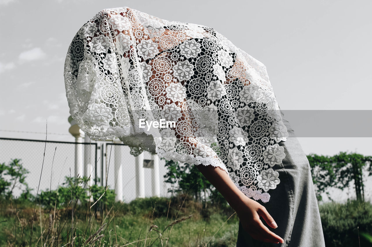 Side view of young woman covered with scarf against sky