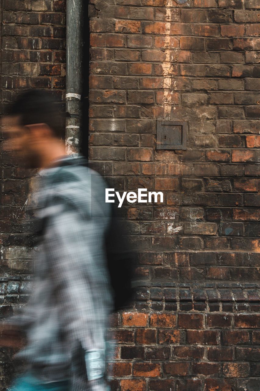 Blurred motion of man walking against brick wall