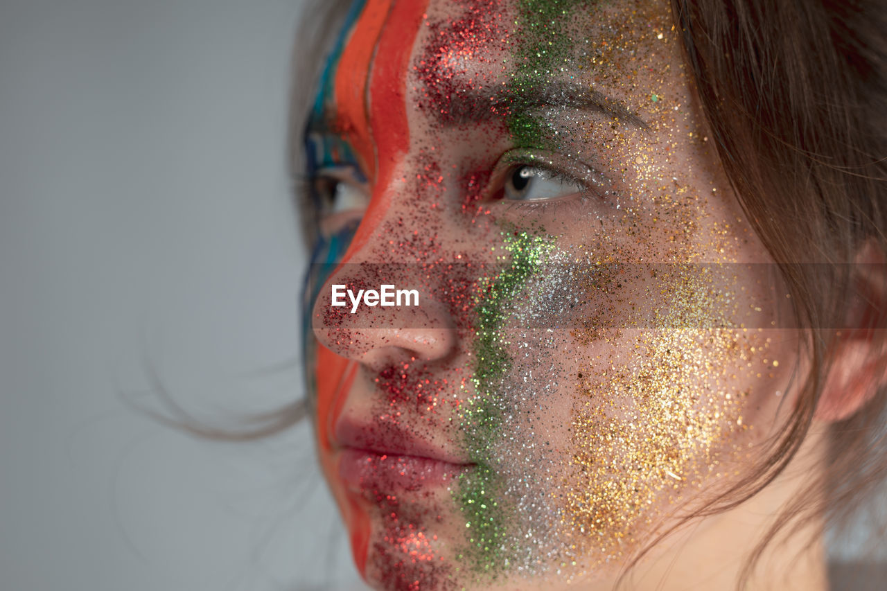 Thoughtful young woman with painted face against gray background