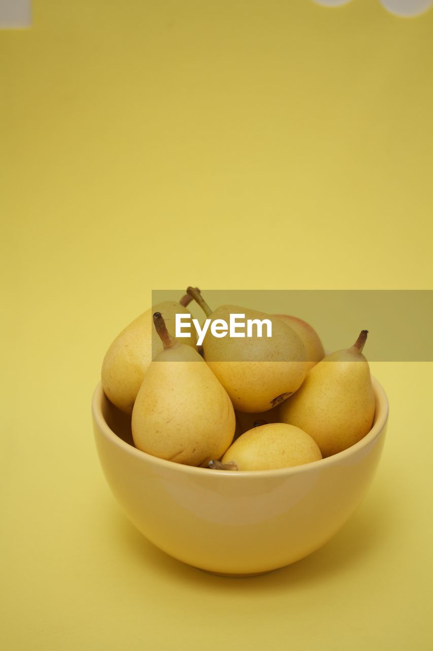 Pears in a yellow bowl on yellow background