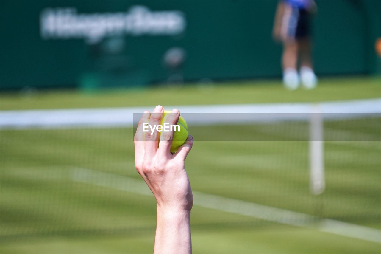 Cropped hand of tennis player throwing ball in court