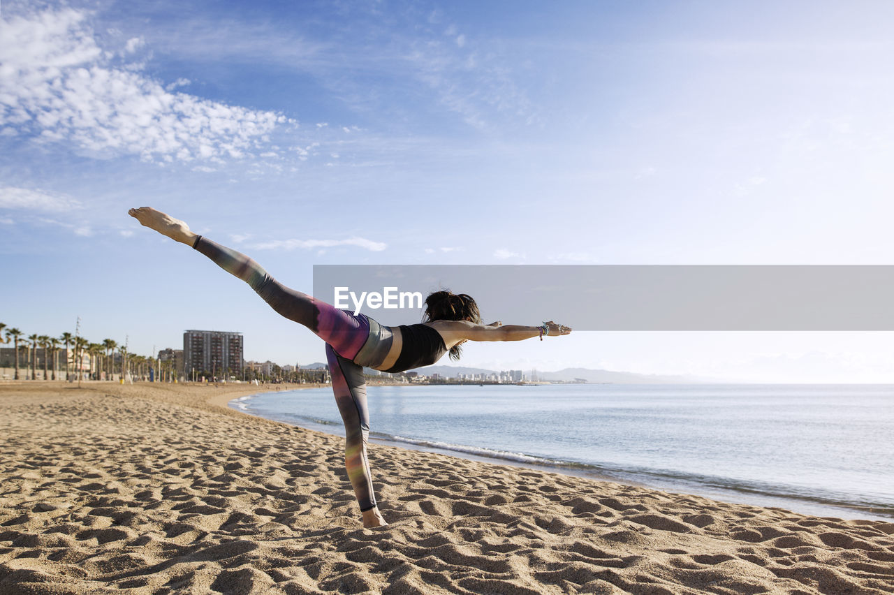 Determined woman performing yoga in warrior 3 pose on beach