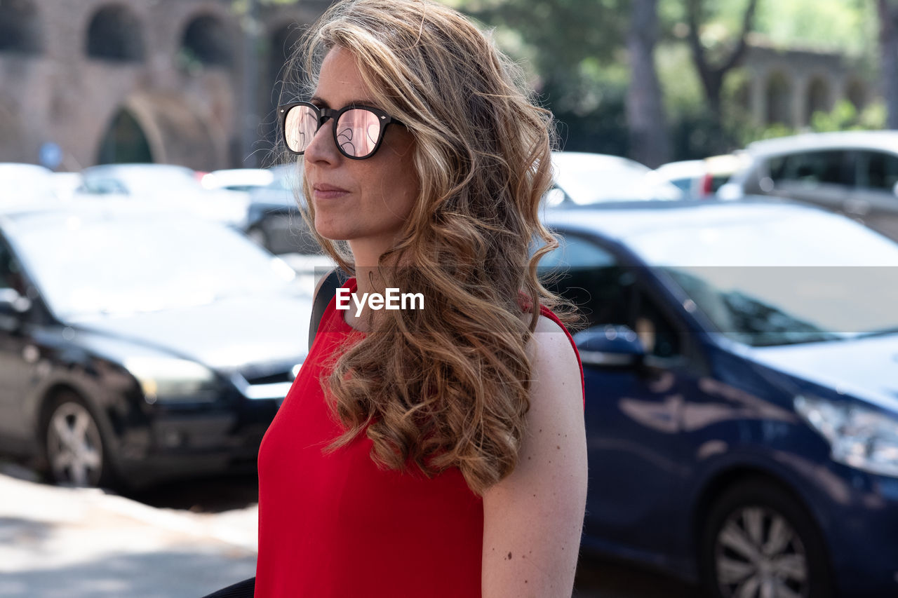 Woman wearing sunglasses while standing against cars