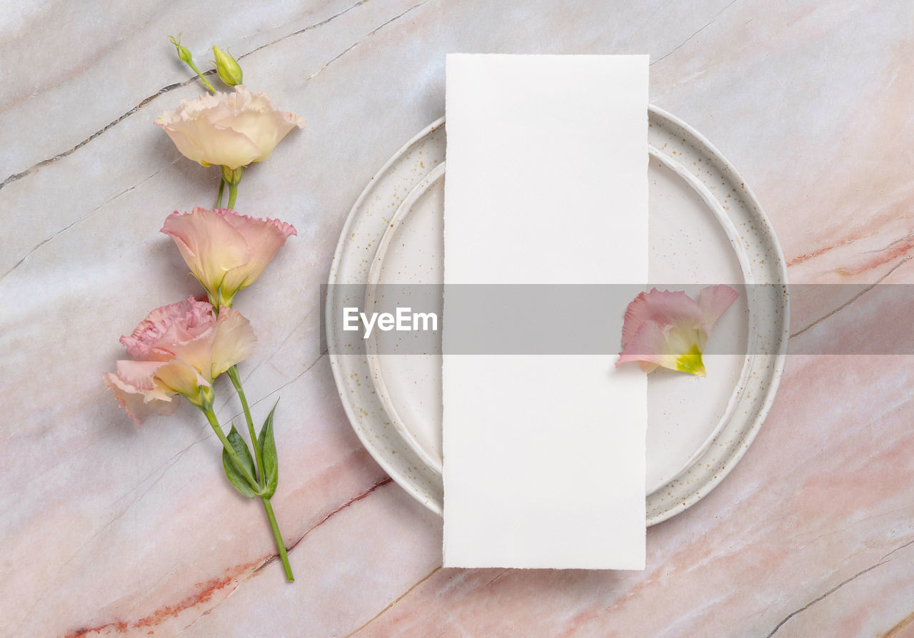 Wedding menu laying on a ceramic plate on a marble table decorated with flowers and ribbons