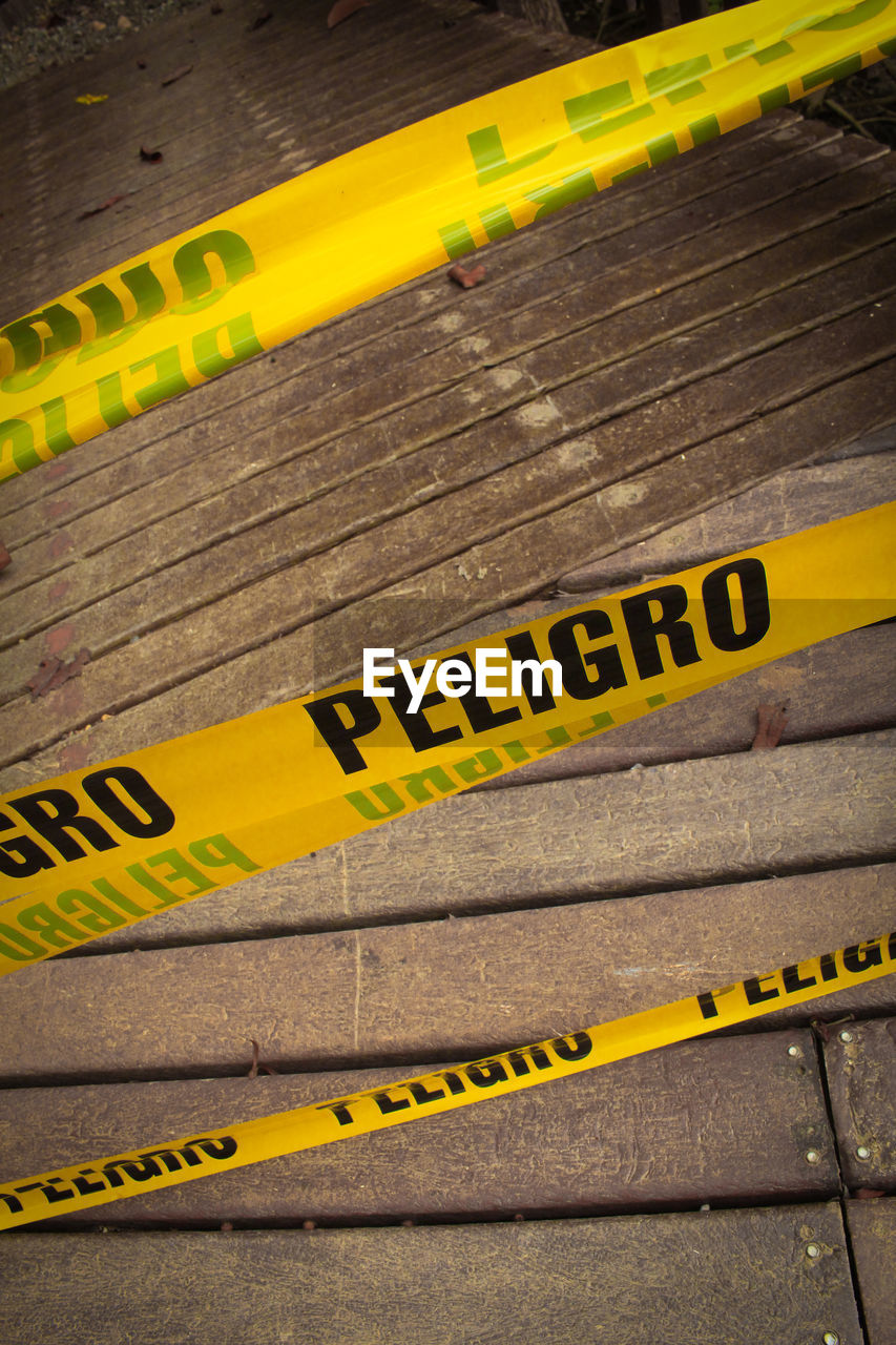 High angle view of yellow cordon tapes over wooden footpath