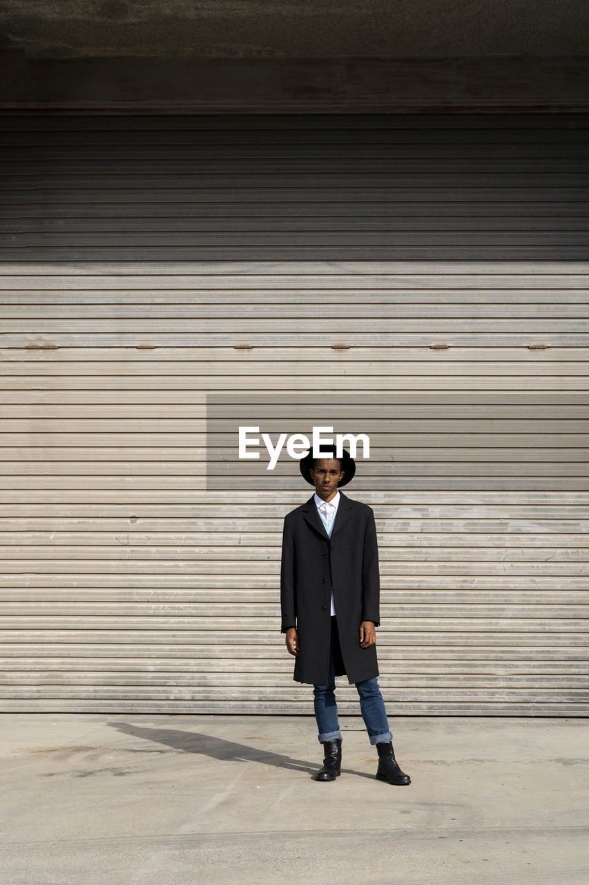 Fashionable young man standing against shutter on sunny day