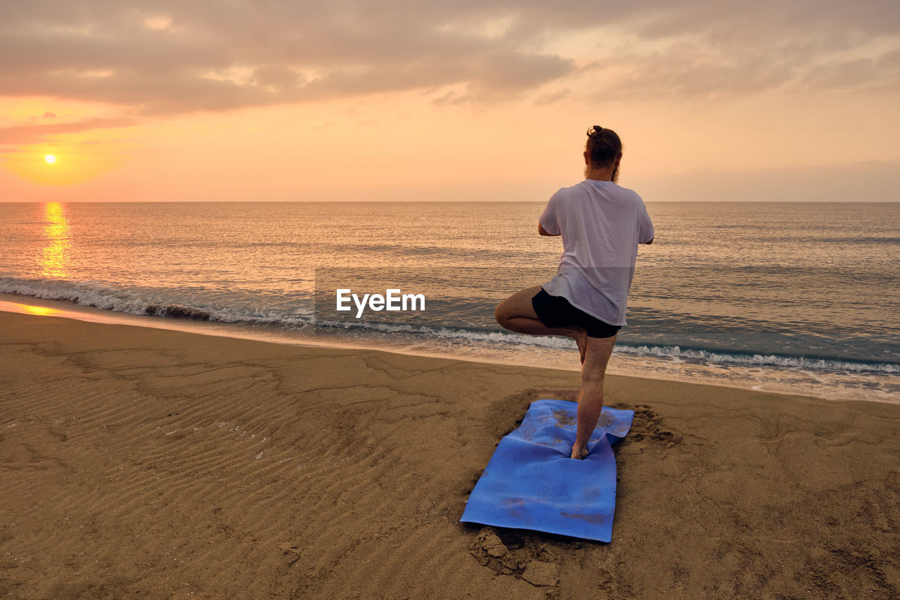 Man stands balancing in tree pose asana at beach during sunrise. yoga practices. getting balance