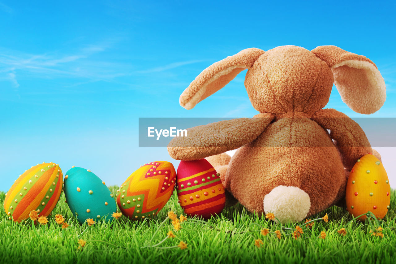 Stuffed toy with easter eggs on grassy land against sky