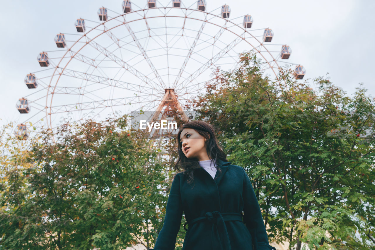 LOW ANGLE VIEW OF WOMAN STANDING IN PARK AGAINST SKY