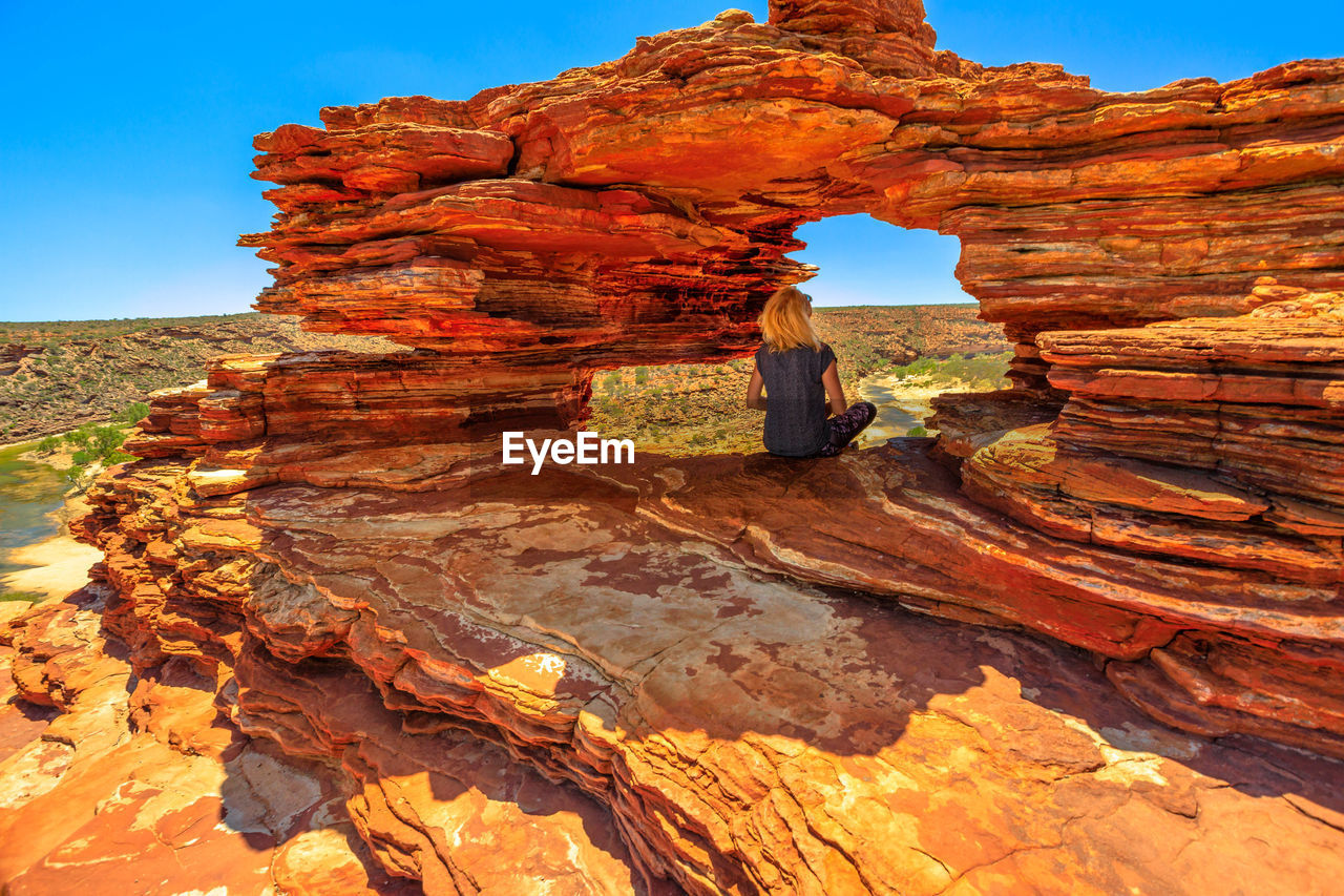 Rear view of woman sitting on rock formation at kalbarri national park 