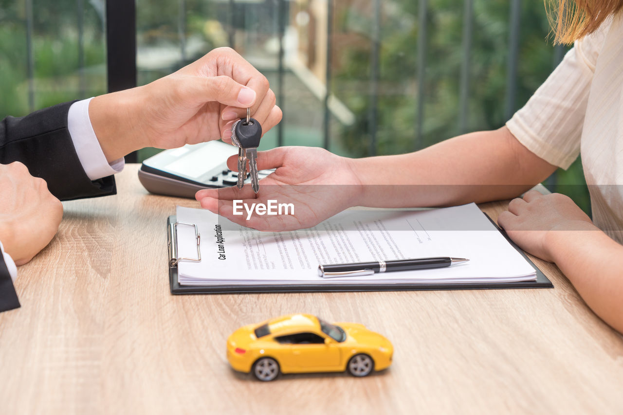 Cropped hand of businessman giving car keys to customer at desk in office