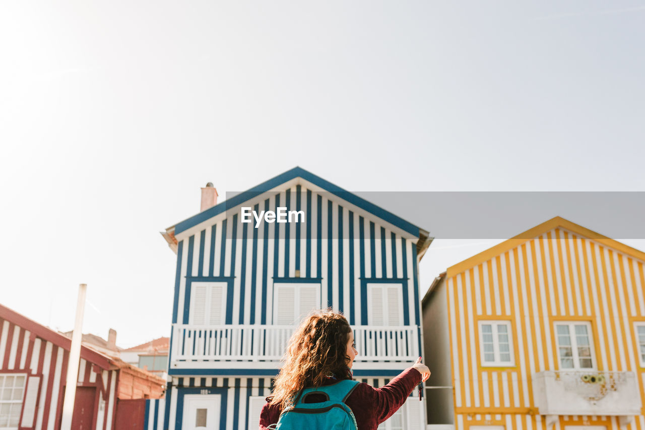 Back view of backpacker woman in front of colorful houses.promenade of costa nova, aveiro, portugal
