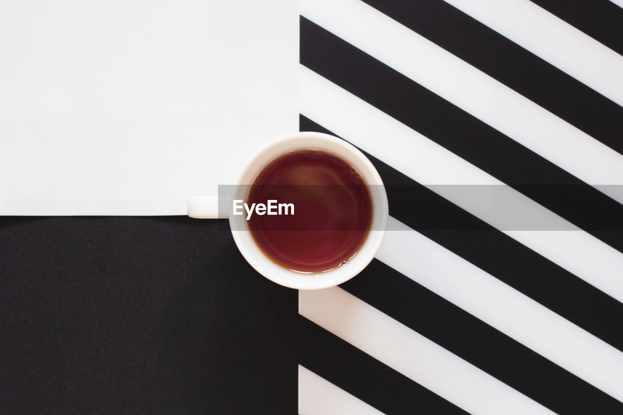 Cup of coffee / tea on black and white table with stripes in minimal style. top view, flat lay