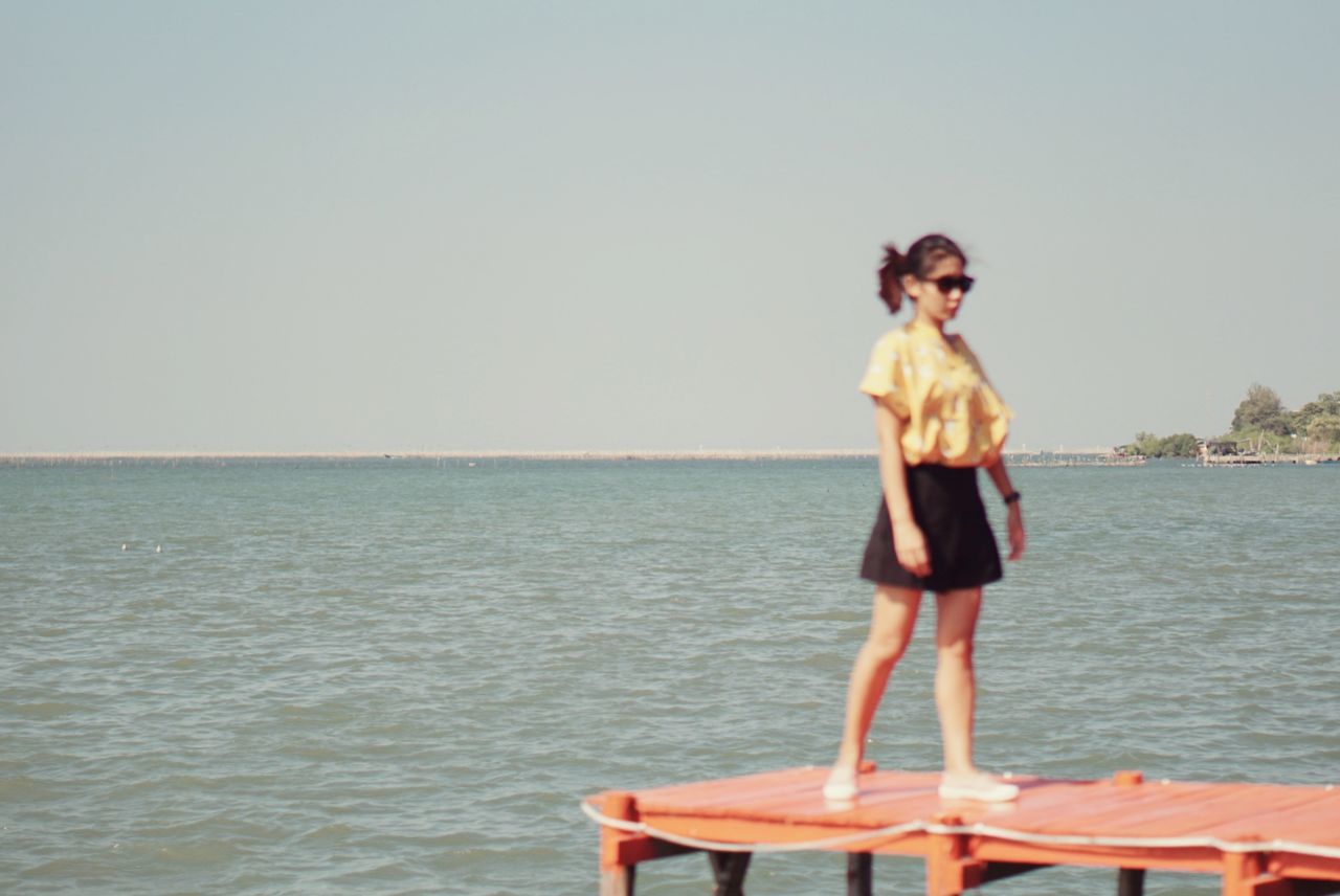 WOMAN STANDING AT BEACH AGAINST CLEAR SKY