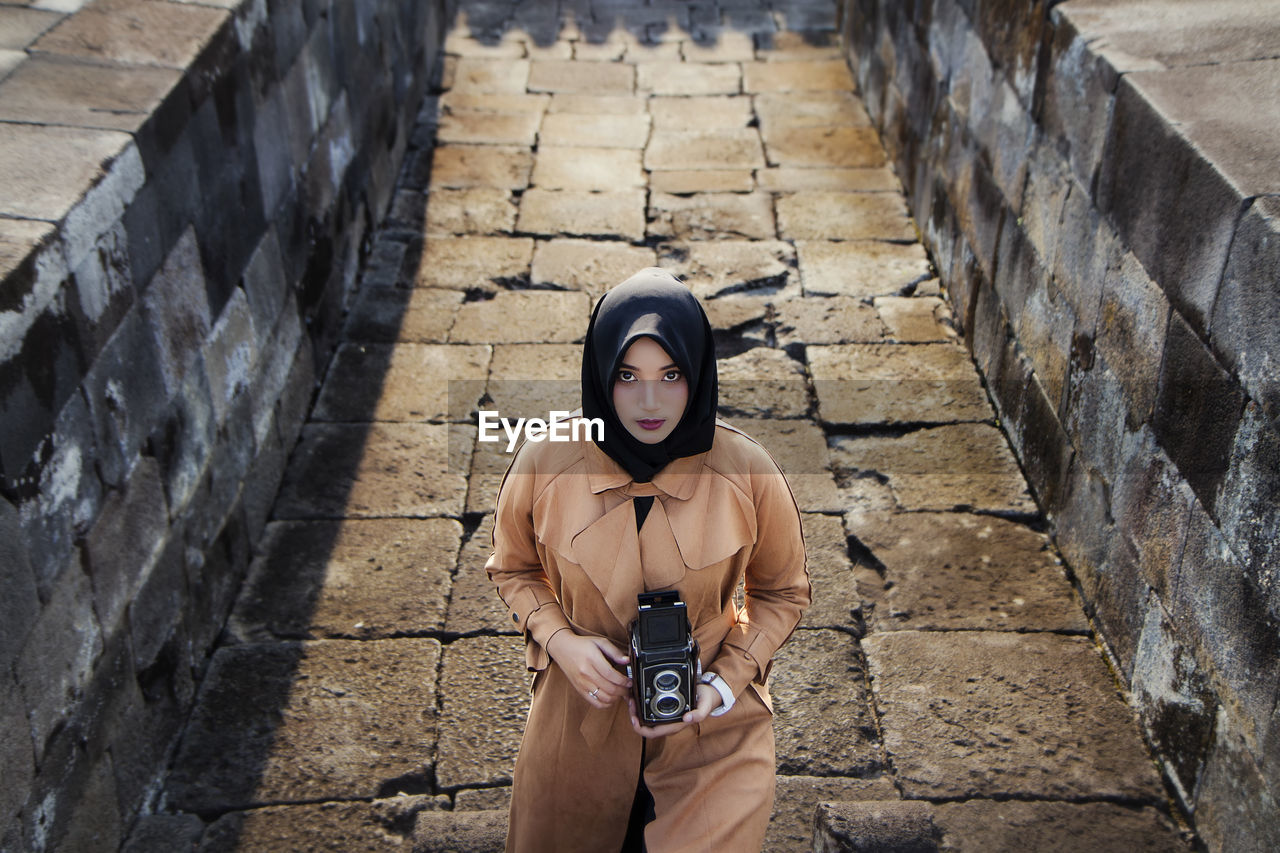 Muslim tourist woman wearing hijab / headscarf and brown coat at ratu boko temple, yogyakarta