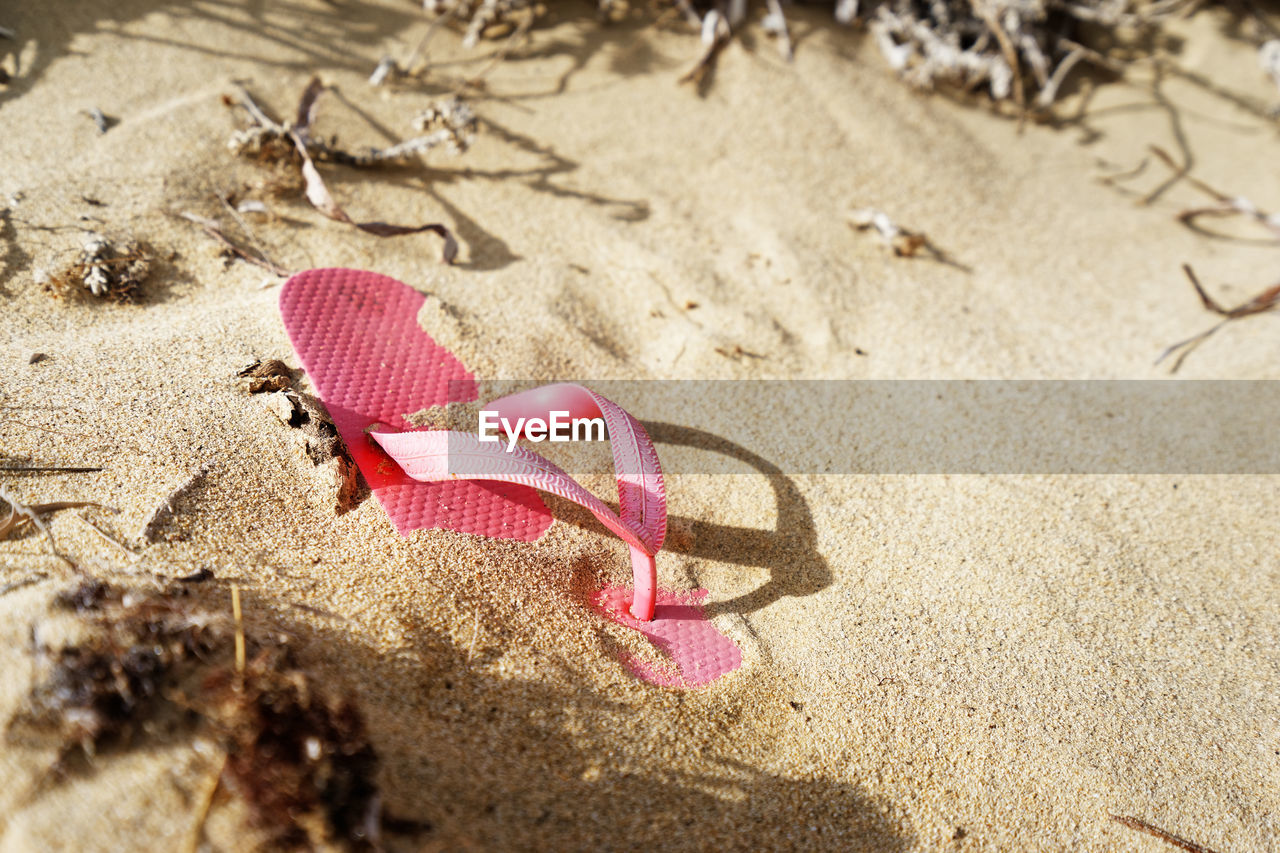 A single pink flip-flop shoe lies deserted on a sandy beach, it is partially covered with sand