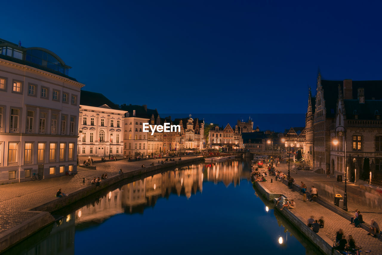 Illuminated buildings by river against sky at night