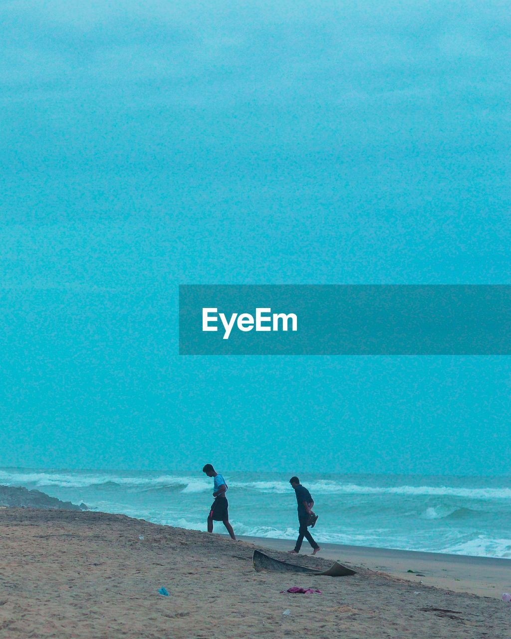 PEOPLE WALKING ON BEACH AGAINST SEA