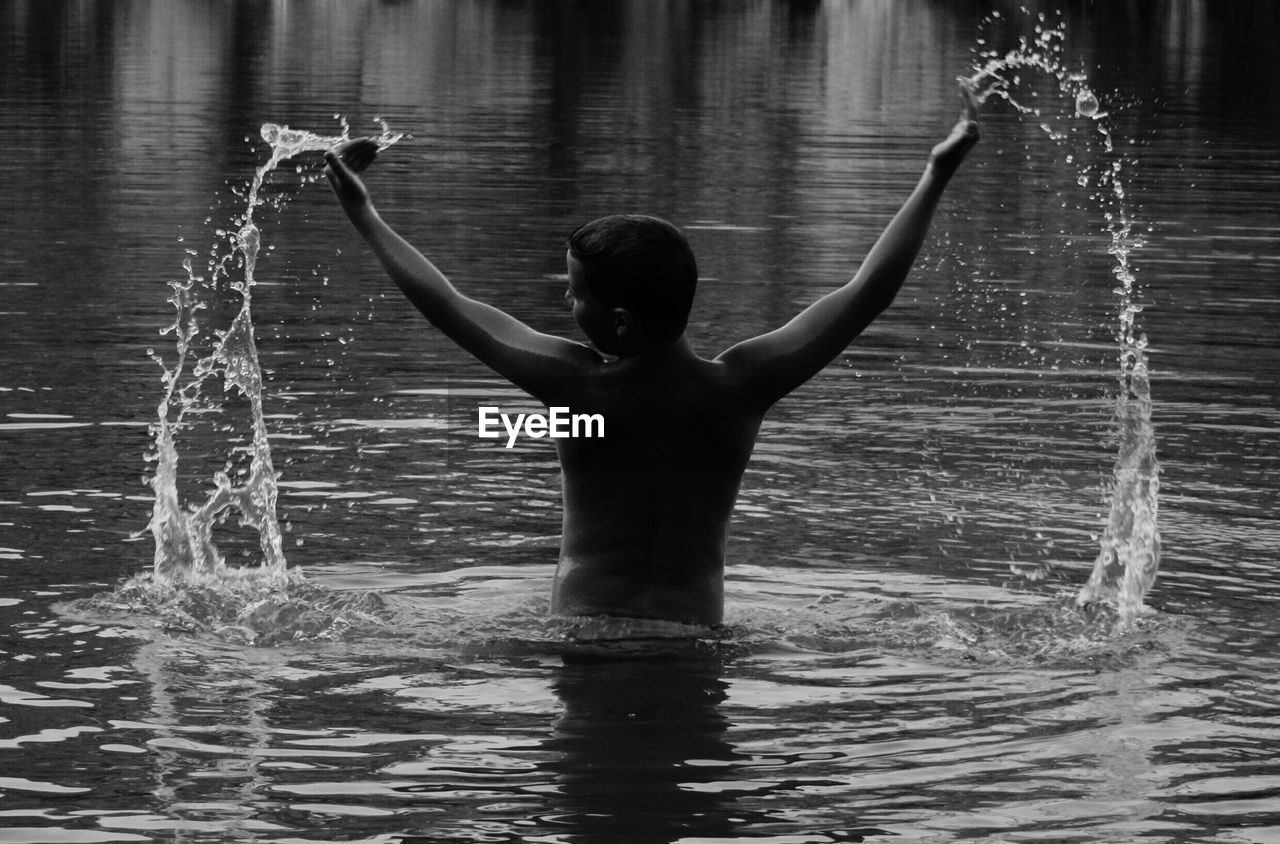 Rear view of shirtless boy playing in river