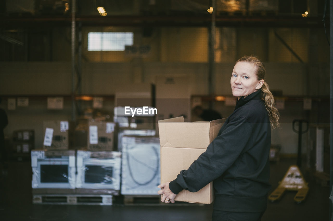 Mature businesswoman carrying box container in logistics warehouse