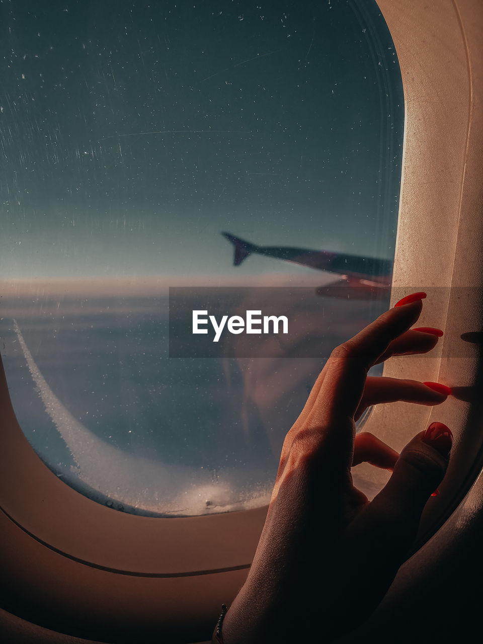 Aerial view of hand against sky seen through airplane window