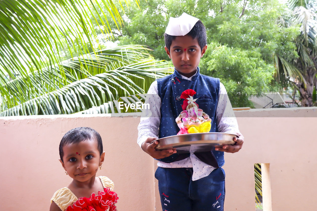 Portrait of boy holding ganesh statue standing at balcony