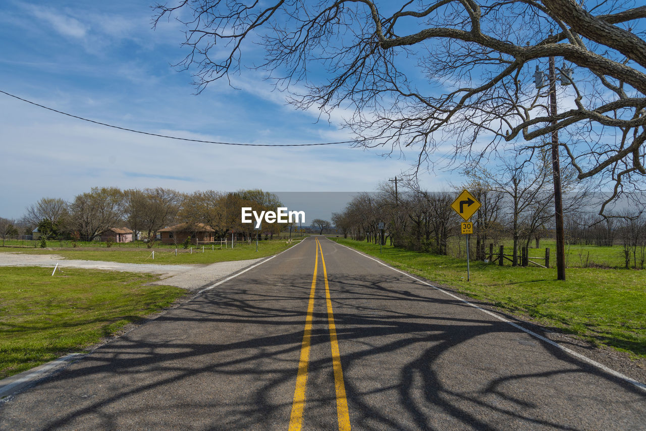 Road sign by trees against sky