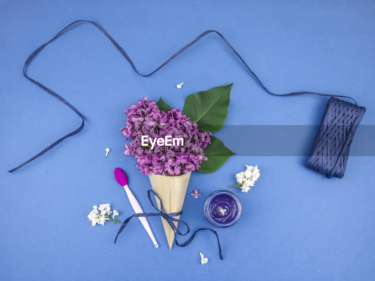 Lilac flowers in a wooden cone, paper tape, cosmetic cream and a brush for masks on a blue.