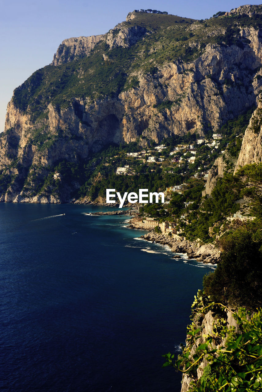 Scenic view of sea by mountain against sky
