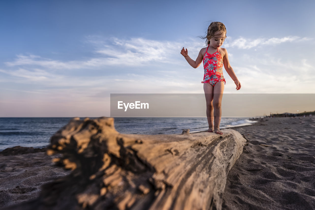 Girl balancing on drift wood log at the beach looks down