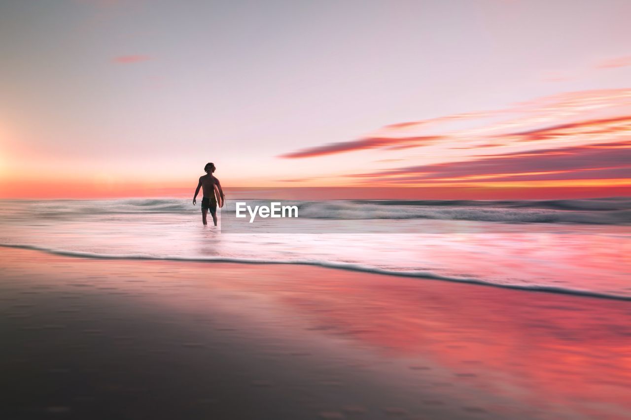 SILHOUETTE PERSON STANDING ON BEACH DURING SUNSET