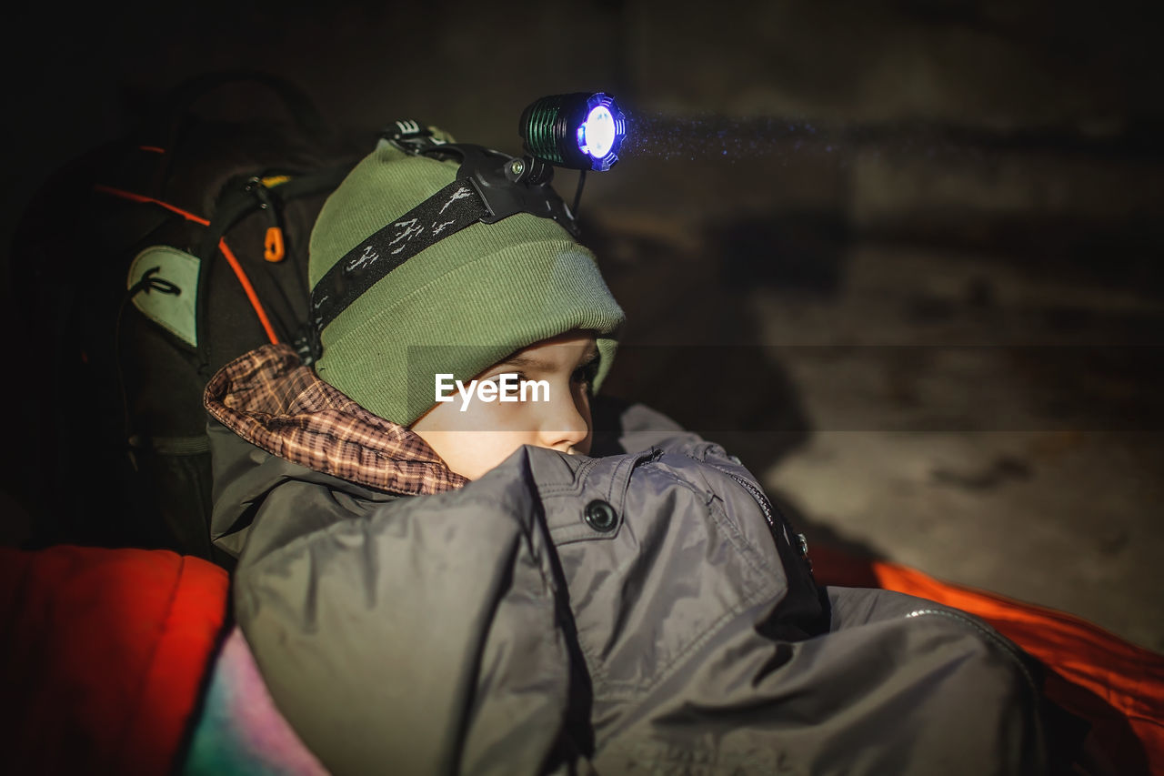 Ukrainian boy with headlamp lay in bomb shelter and waits for end of airstrike of russian invaders